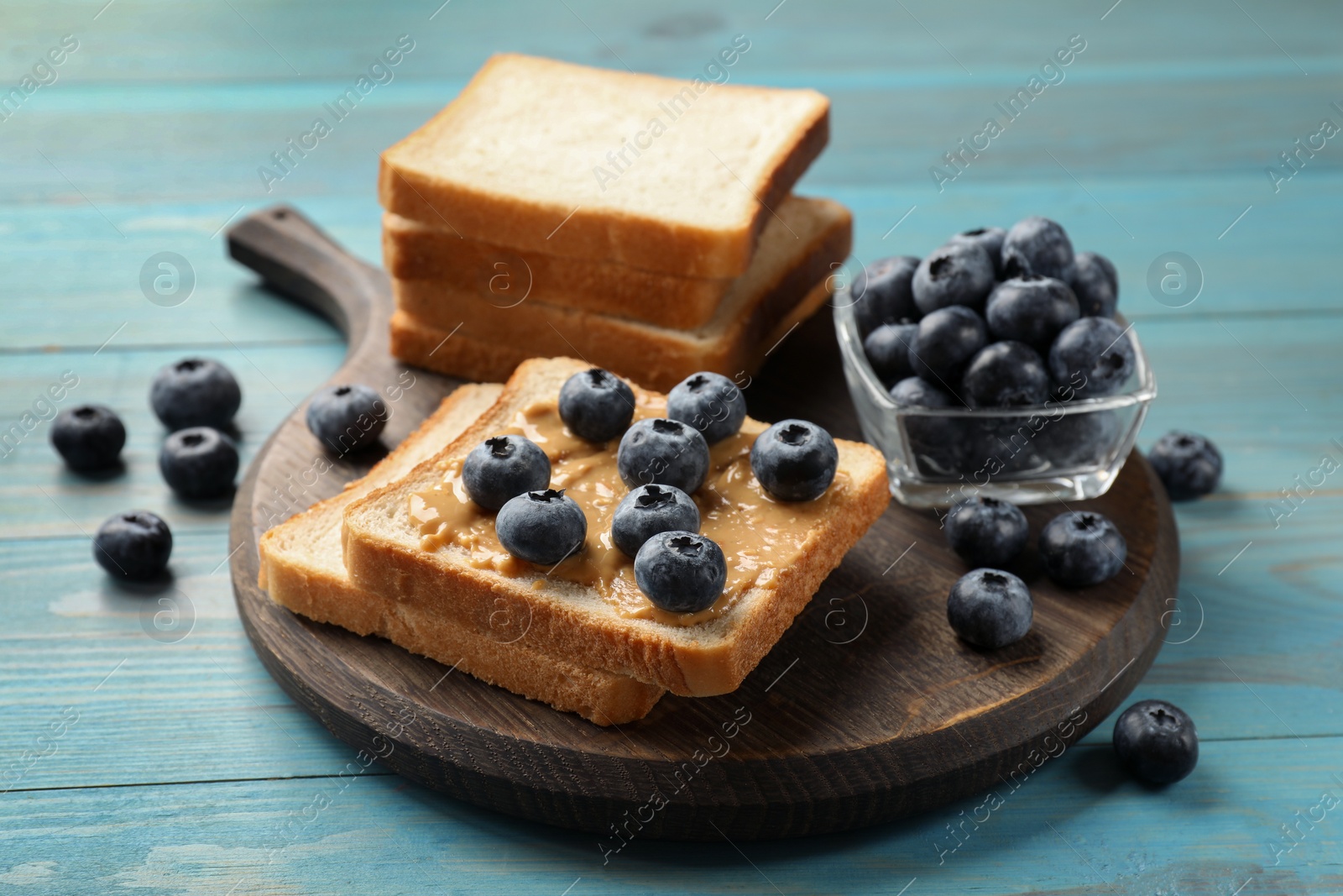 Photo of Delicious toasts with peanut butter and blueberries on light blue wooden table, closeup