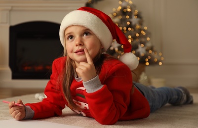 Photo of Cute child writing letter to Santa Claus while lying on floor at home. Christmas celebration