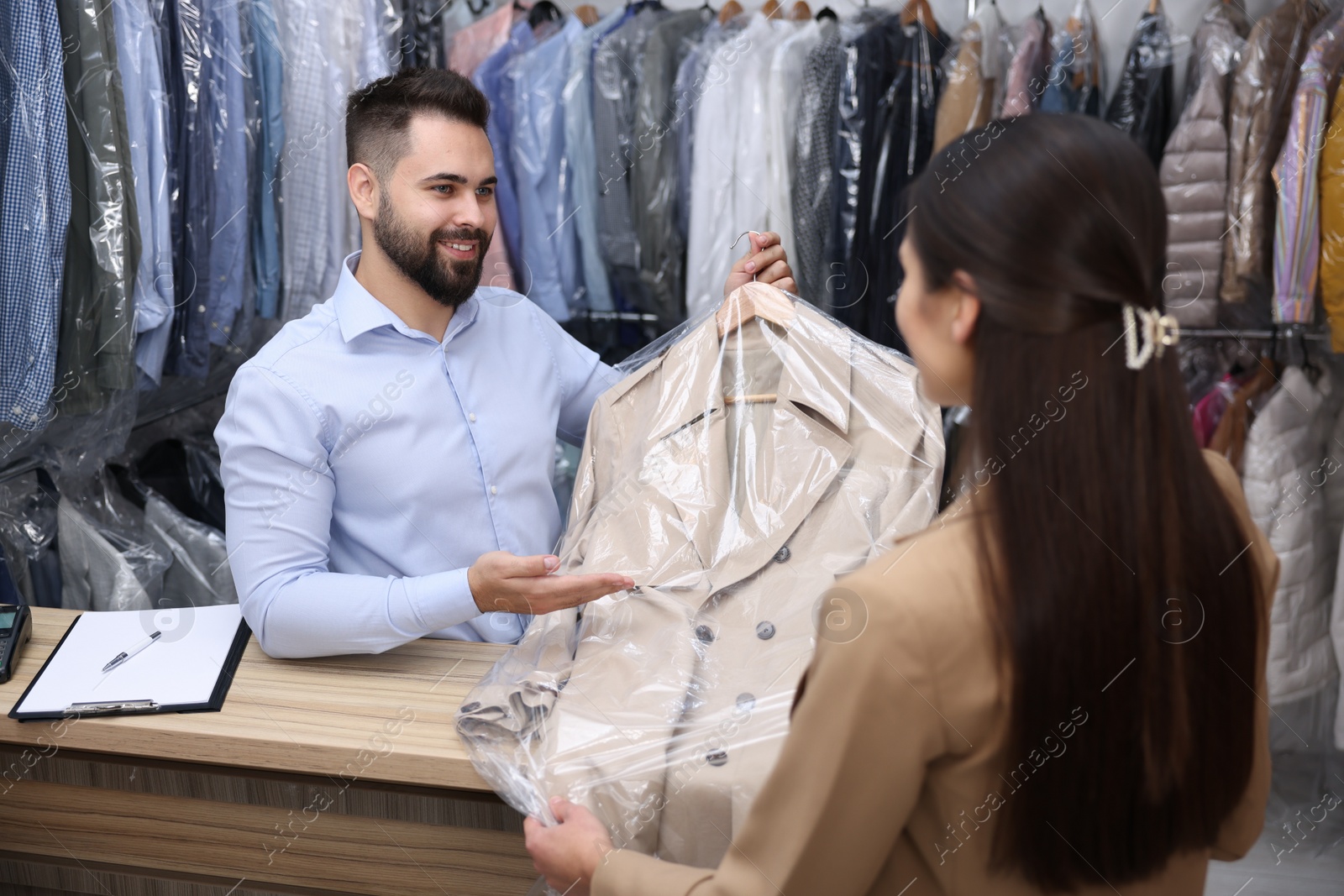 Photo of Dry-cleaning service. Happy worker giving coat to client indoors