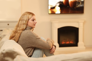 Photo of Beautiful young woman resting near fireplace at home