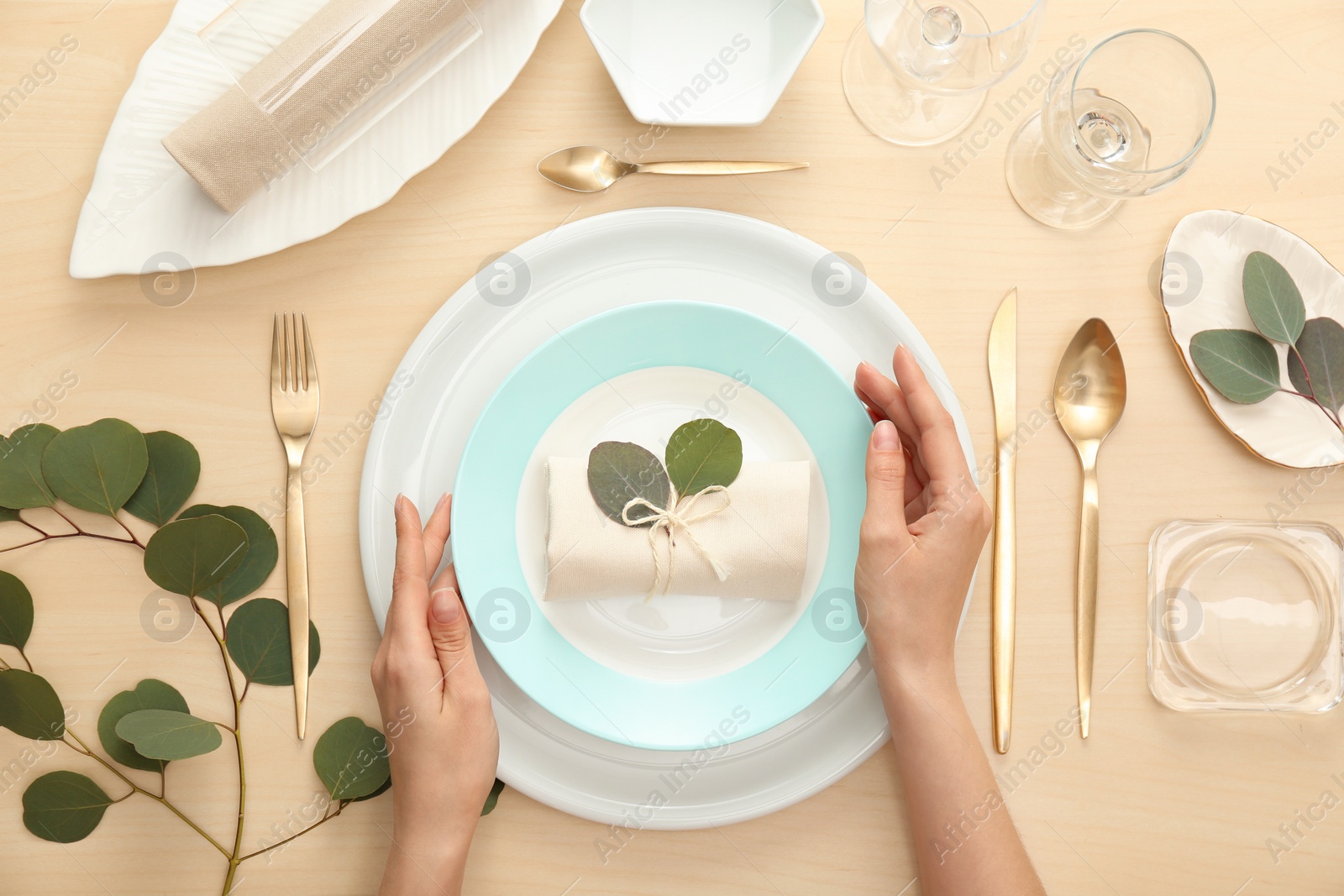 Photo of Woman setting table with green leaves for festive dinner, top view