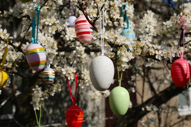 Photo of Beautifully painted Easter eggs hanging on blooming cherry tree outdoors