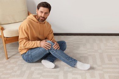 Photo of Man suffering from leg pain on carpet indoors, space for text