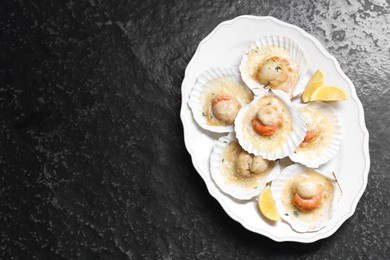 Photo of Fried scallops in shells and lemon on black textured table, top view. Space for text