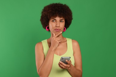 Photo of Thoughtful young woman with smartphone on green background