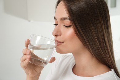 Woman drinking tap water from glass at home, closeup
