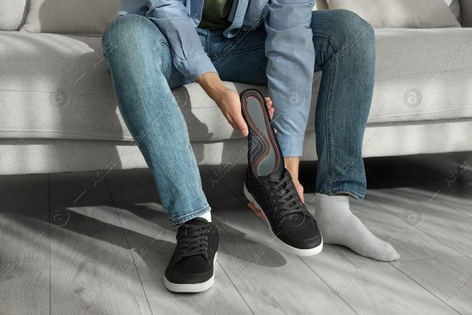 Photo of Man putting orthopedic insole into shoe indoors, closeup