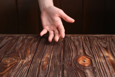 Photo of Woman holding hand above wooden table, selective focus. Space for text