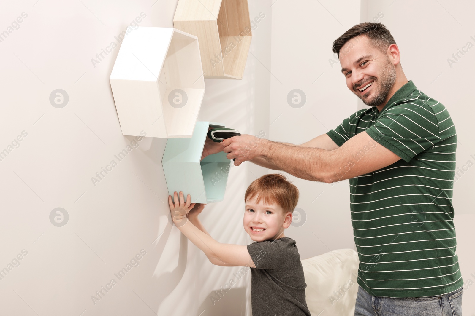 Photo of Father and son installing shelves on wall indoors. Repair work