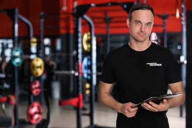 Portrait of professional personal trainer with clipboard in gym. Space for text