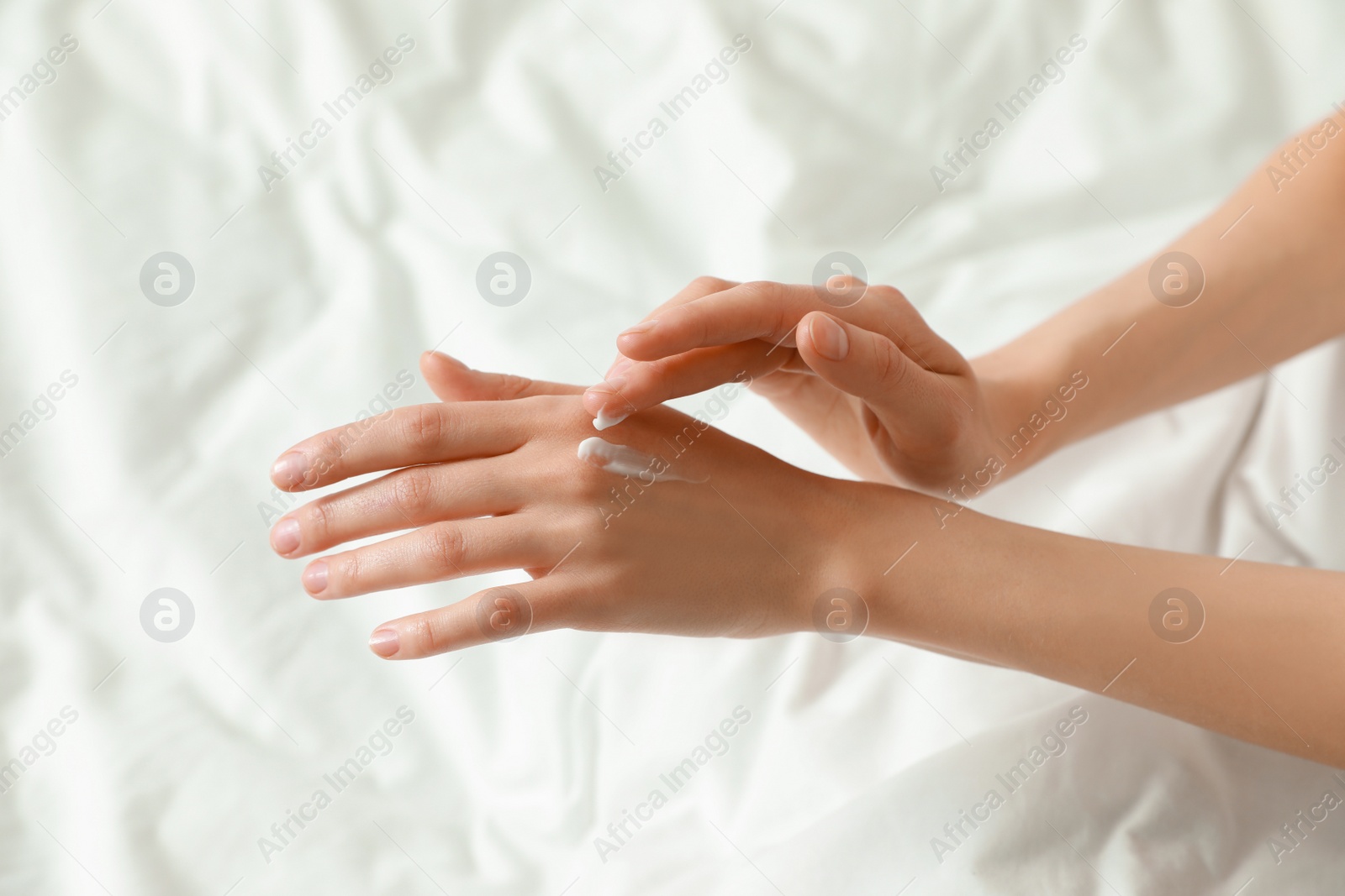 Photo of Woman applying hand cream in bed, closeup