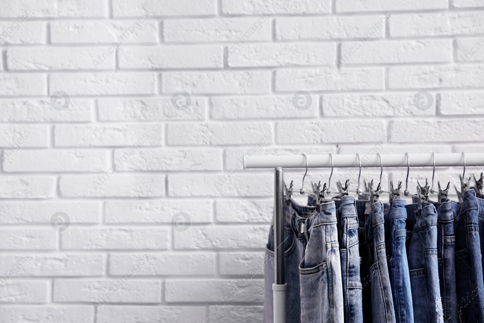 Photo of Rack with stylish jeans near brick wall. Space for text