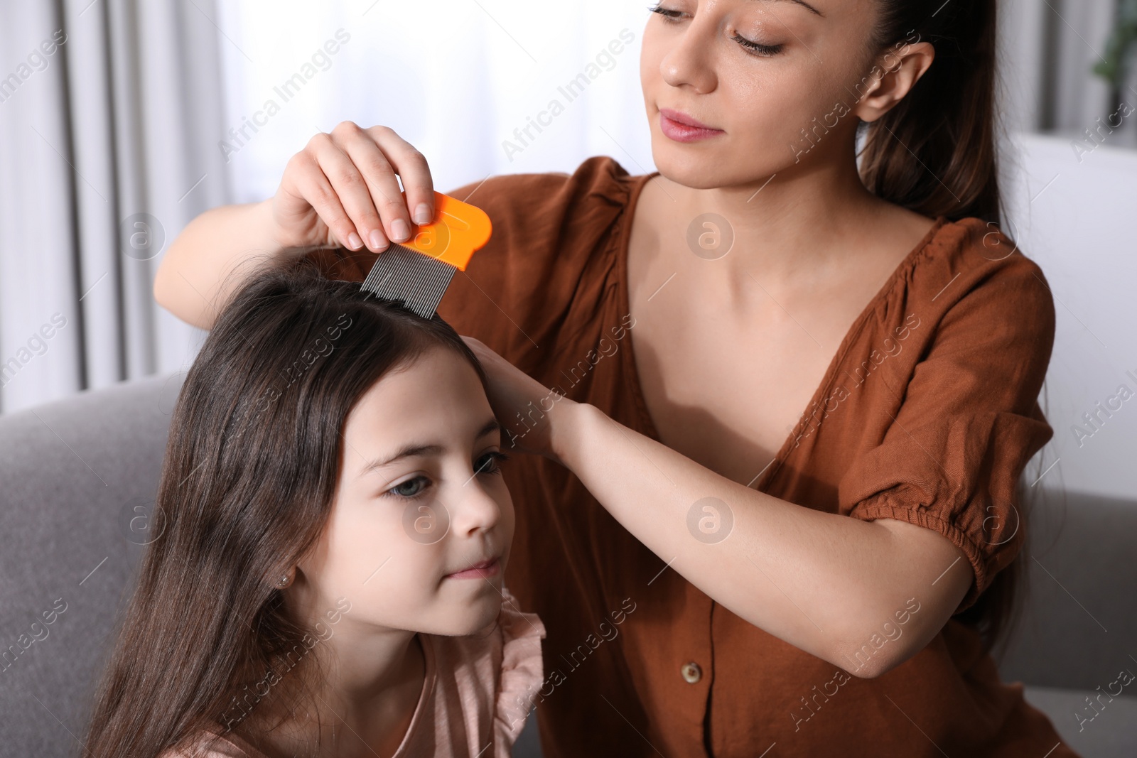 Photo of Mother using nit comb on her daughter's hair indoors. Anti lice treatment