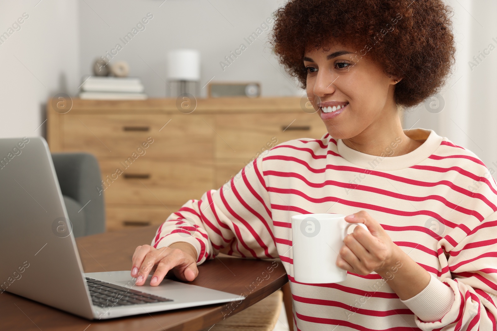 Photo of Beautiful young woman using laptop and drinking coffee at wooden table in room