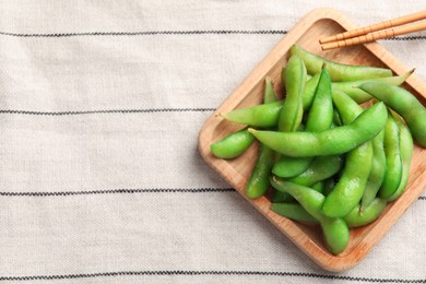 Photo of Wooden plate with green edamame beans in pods and chopsticks on towel, top view. Space for text