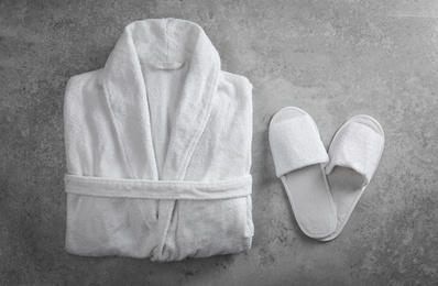 Photo of Clean folded bathrobe and slippers on grey stone background, flat lay