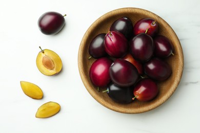 Bowl with tasty ripe plums on white marble table, flat lay