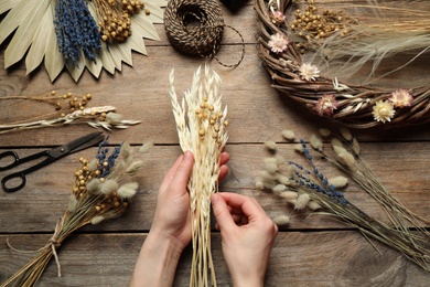Photo of Florist making bouquet of dried flowers at wooden table, top view