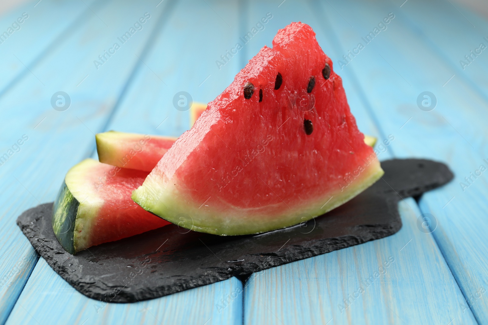 Photo of Slate board with slices of juicy watermelon on light blue wooden table