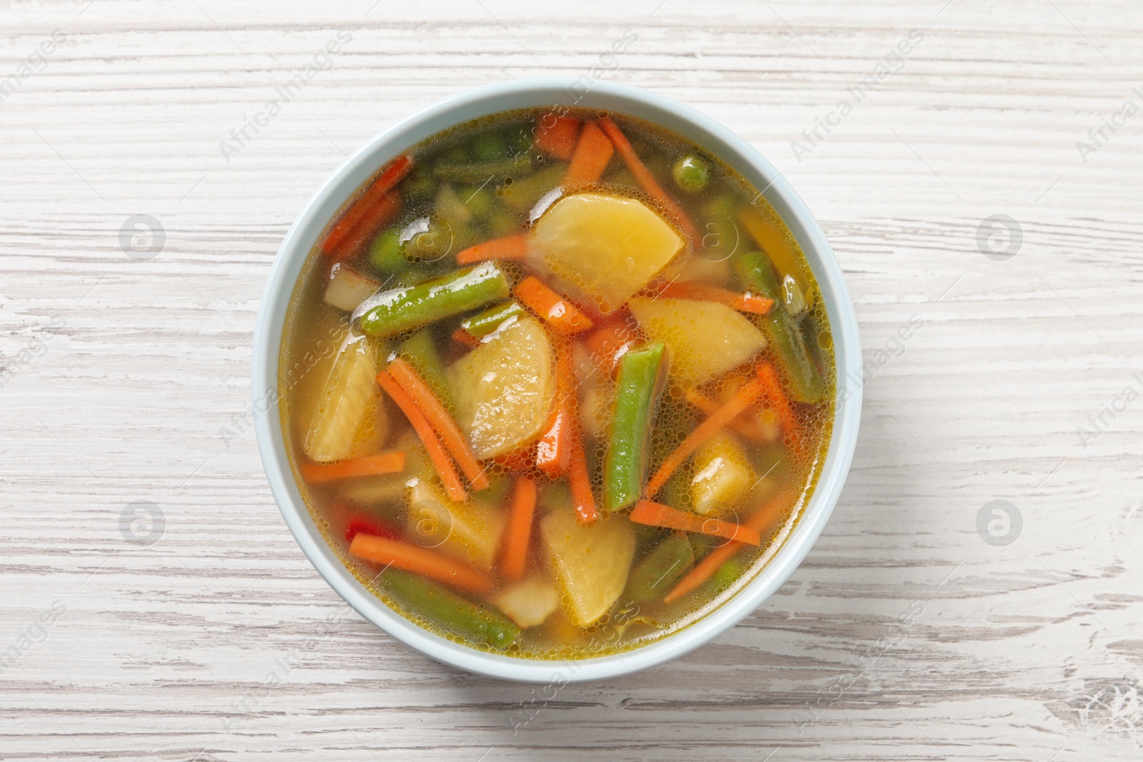 Photo of Bowl of tasty turnip soup on white wooden table, top view