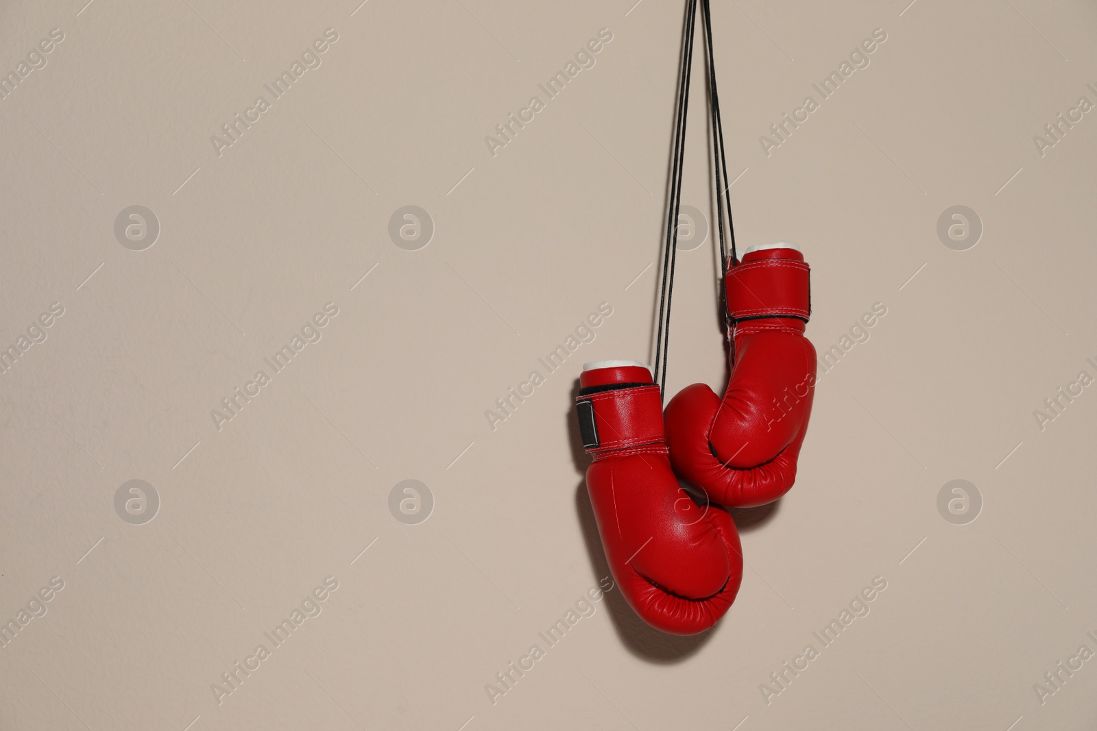 Photo of Pair of boxing gloves hanging on beige wall, space for text