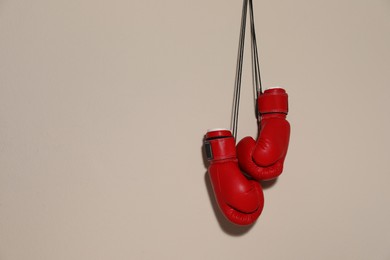 Photo of Pair of boxing gloves hanging on beige wall, space for text