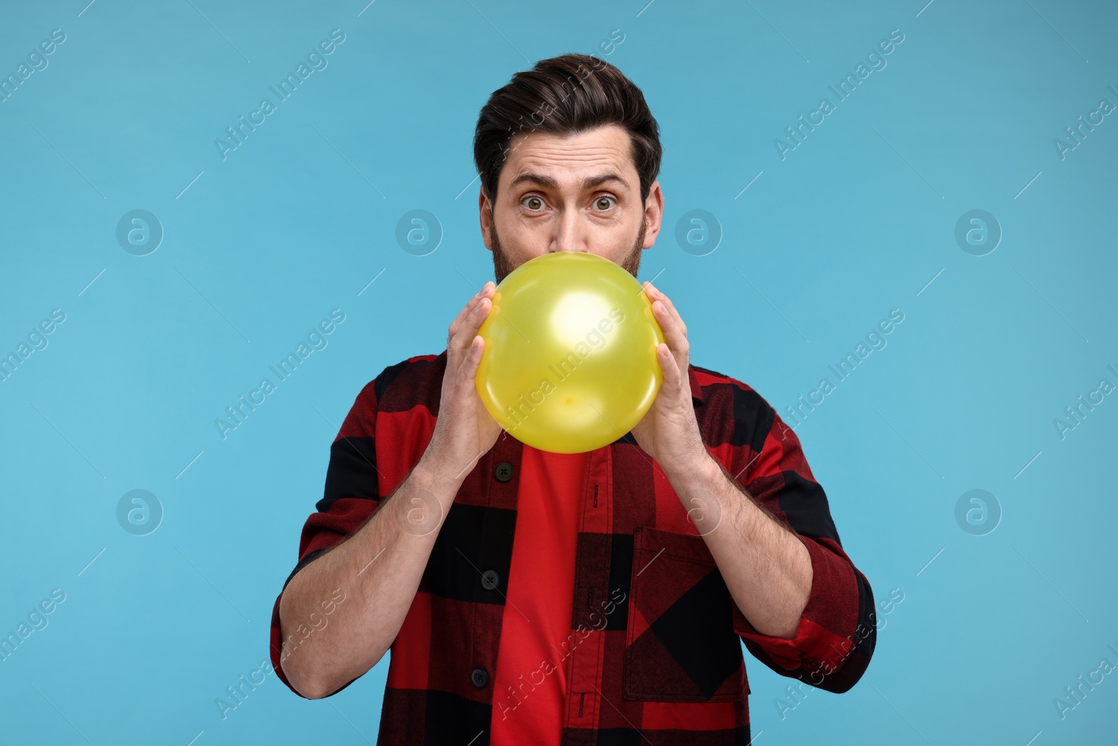 Photo of Man inflating yellow balloon on light blue background