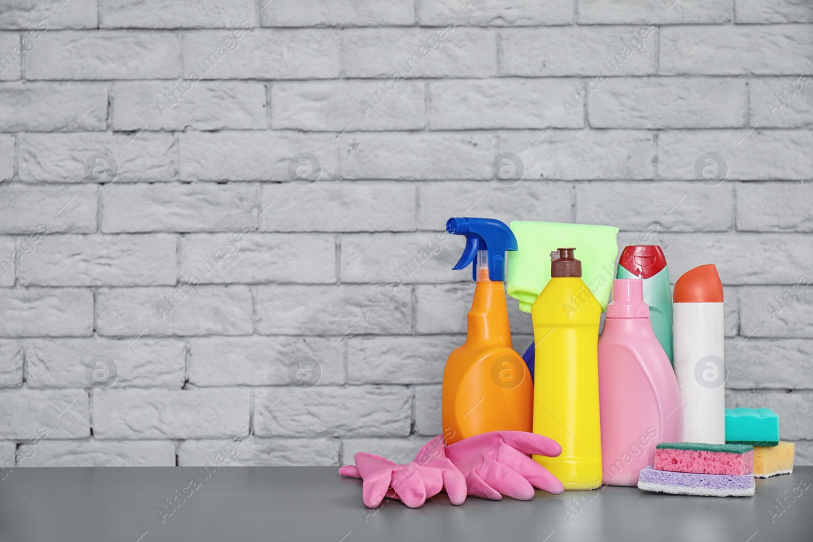 Photo of Set of cleaning supplies on table near brick wall