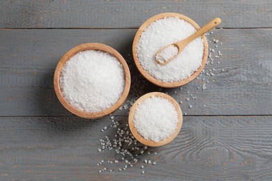 Photo of Bowls of natural sea salt on grey wooden table, flat lay