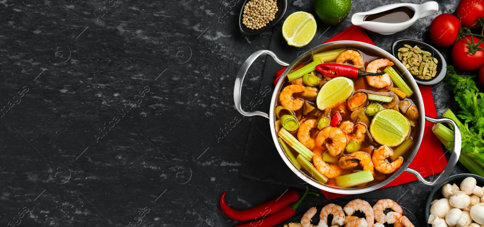 Photo of Saucepan with delicious Tom Yum soup and ingredients on black marble table, flat lay. Space for text