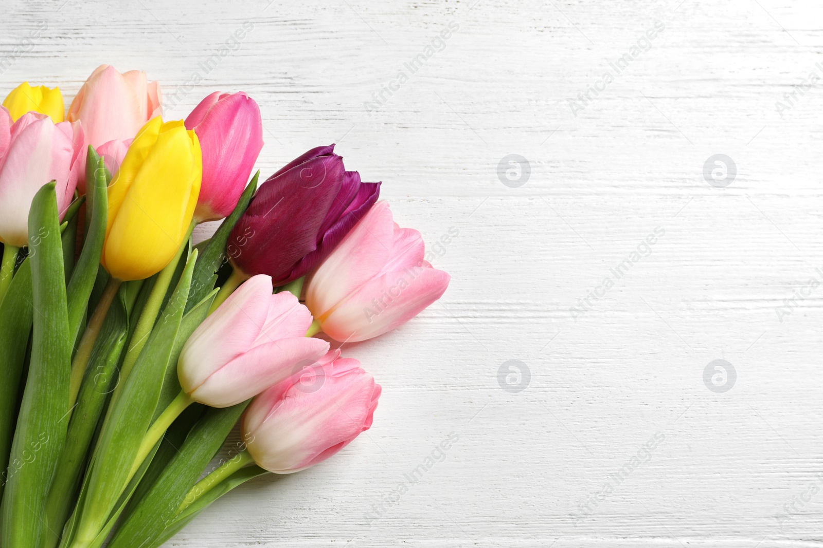 Photo of Beautiful spring tulips on light wooden background, top view with space for text. International Women's Day