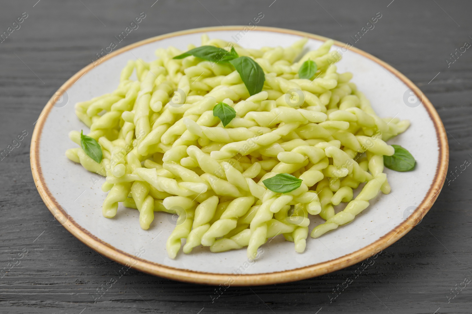 Photo of Plate of delicious trofie pasta with basil leaves on grey wooden table