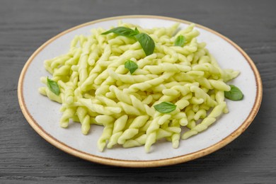 Plate of delicious trofie pasta with basil leaves on grey wooden table