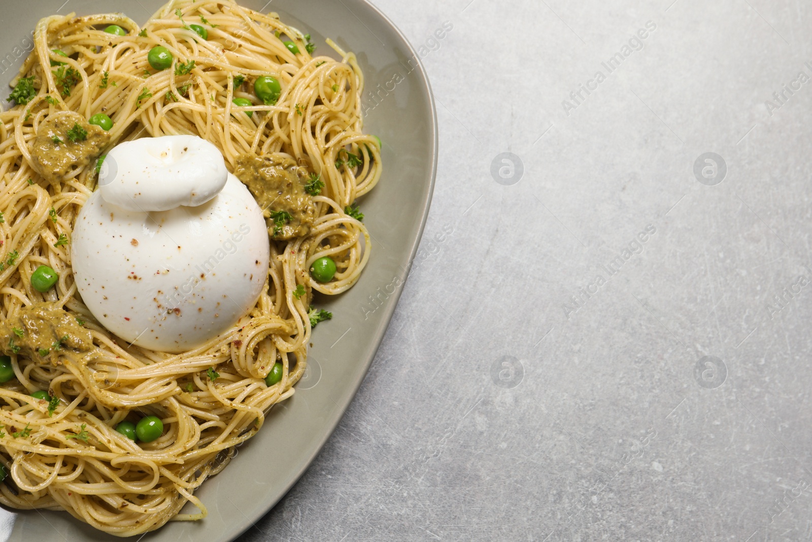 Photo of Delicious spaghetti pasta with burrata cheese, peas and pesto sauce on light grey table, top view. Space for text