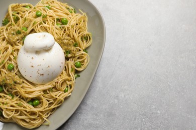 Photo of Delicious spaghetti pasta with burrata cheese, peas and pesto sauce on light grey table, top view. Space for text