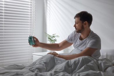 Photo of Sleepy man turning off alarm clock on nightstand in morning