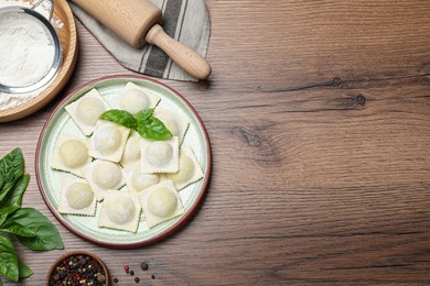 Photo of Uncooked ravioli, basil and peppercorns on wooden table, flat lay. Space for text