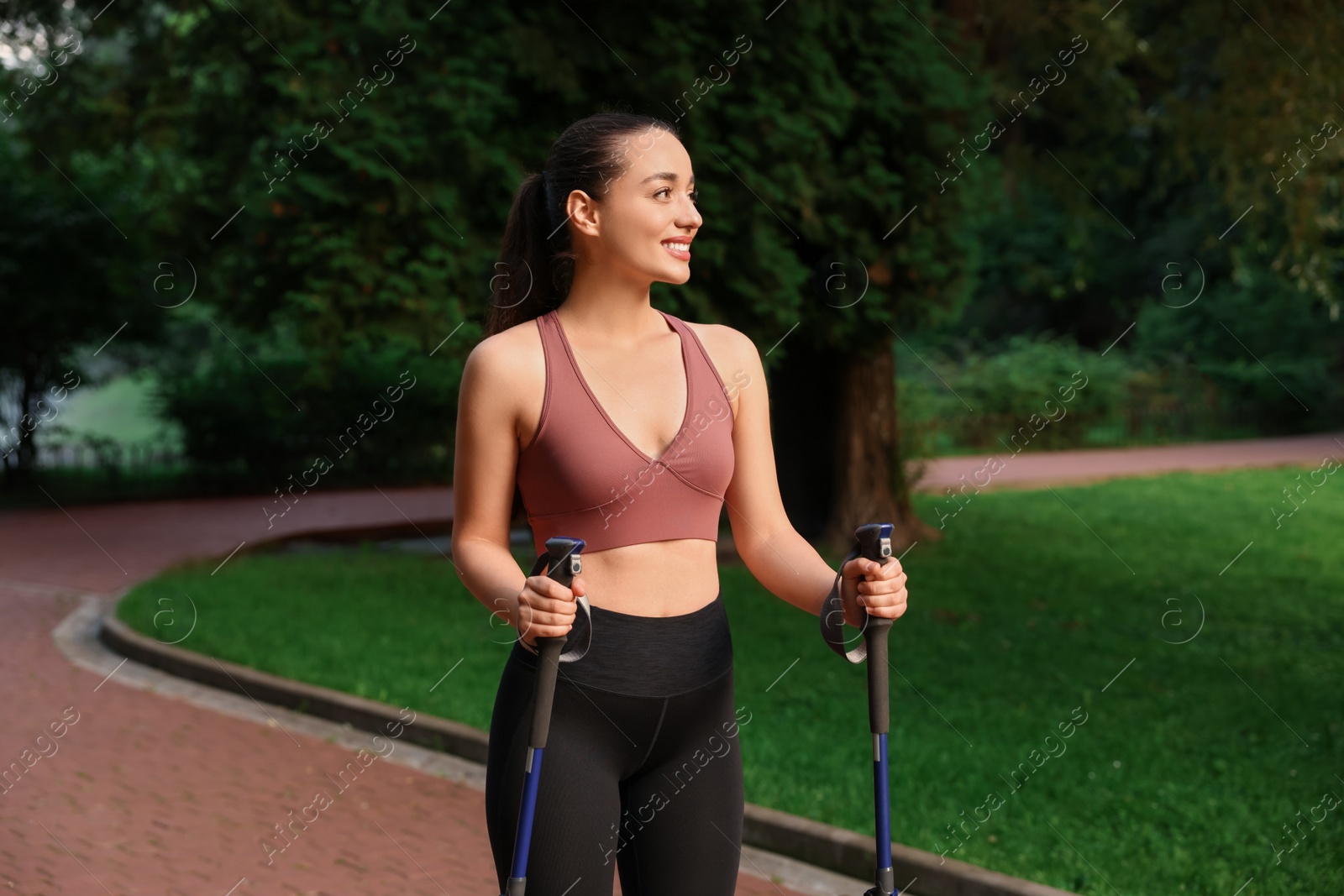 Photo of Young woman practicing Nordic walking with poles outdoors