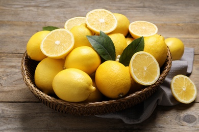 Photo of Many fresh ripe lemons with green leaves on wooden table