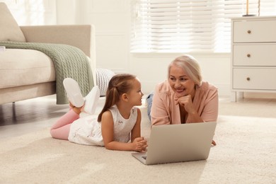 Photo of Happy grandmother and her granddaughter using  laptop together on floor at home