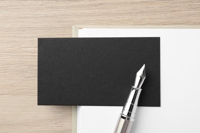 Photo of Blank black business card, fountain pen and notebook on wooden table, top view. Mockup for design