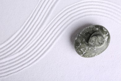 Photo of Zen garden stones on white sand with pattern, top view. Space for text