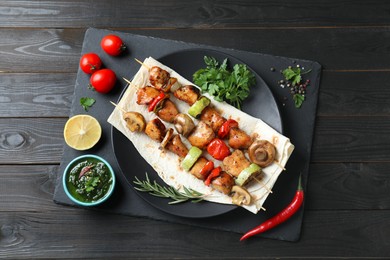 Photo of Delicious shish kebabs with vegetables served on black wooden table, top view