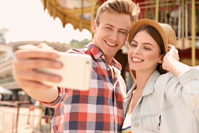Photo of Young happy couple taking selfie near carousel in amusement park