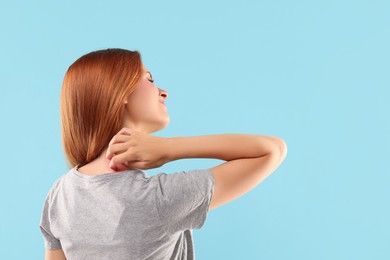 Suffering from allergy. Young woman scratching her neck on light blue background, space for text