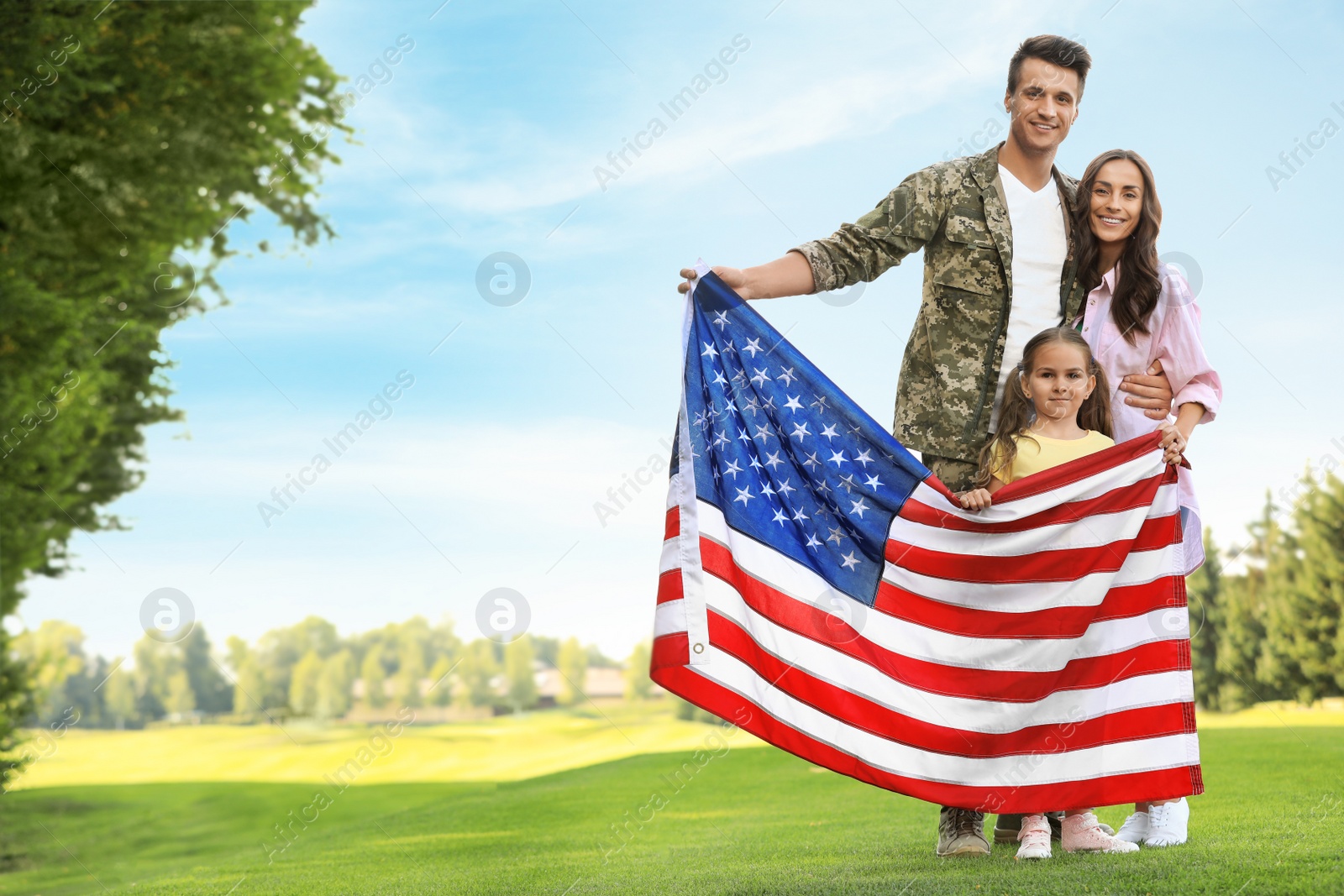 Photo of Man in military uniform with American flag and his family at sunny park