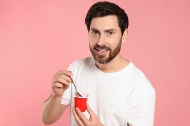 Handsome man with delicious yogurt and spoon on pink background