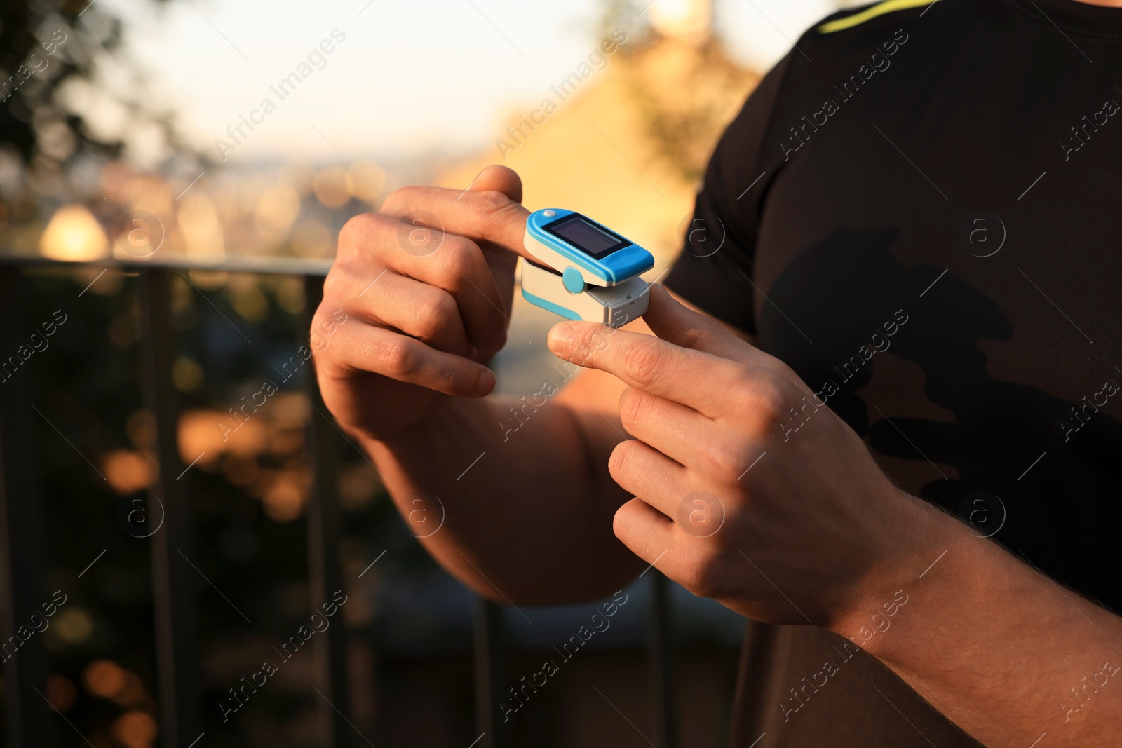 Photo of Man checking pulse with blood pressure monitor on finger after training outdoors, closeup