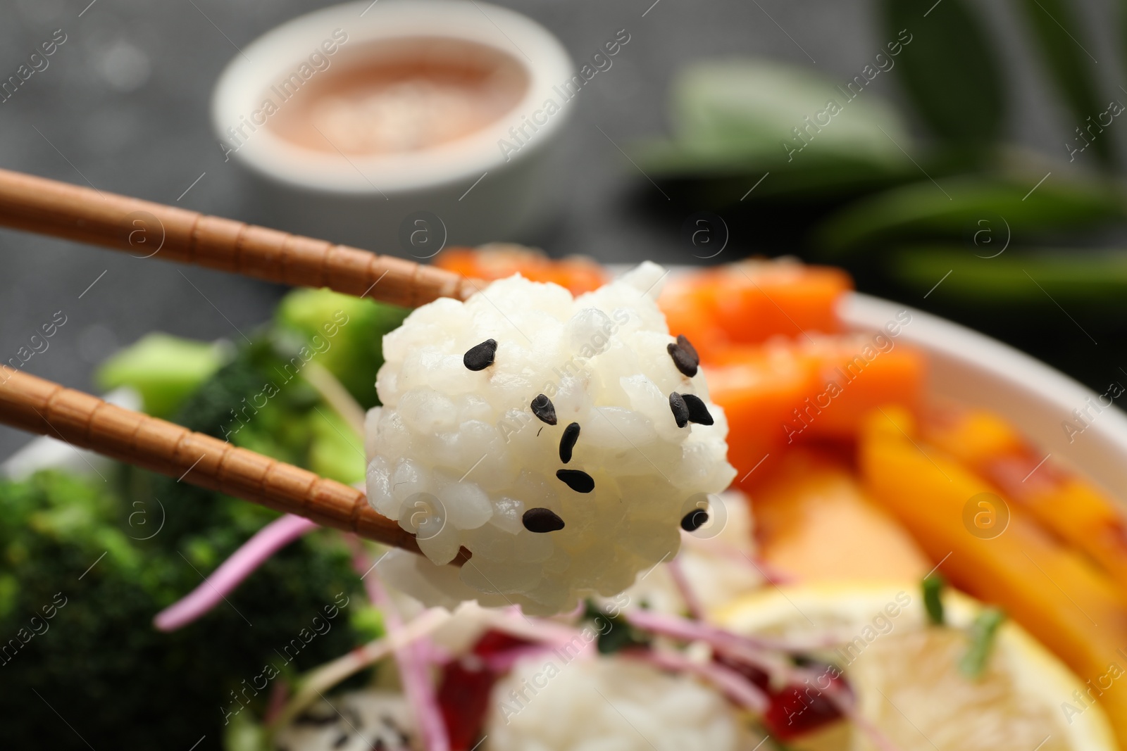 Photo of Holding rice with chopsticks over bowl at grey table, closeup. Vegan diet