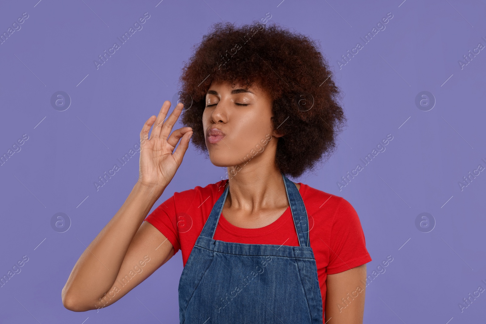 Photo of Happy young woman in apron showing perfect sign on purple background